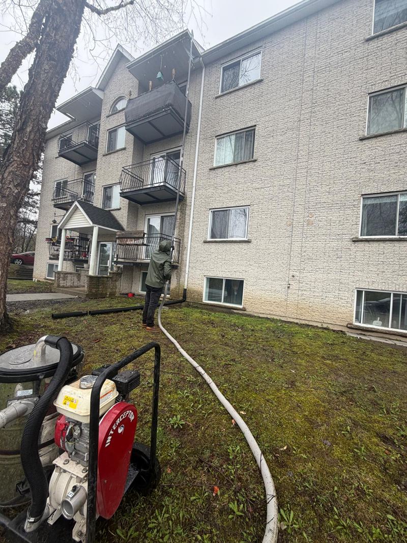 L’aspirateur à gouttières sur la pelouse&nbsp;: moteur rouge, baril d’acier, boyau noir. Au fond, l’opérateur manie la perche contre un immeuble beige de 4&nbsp;étages.